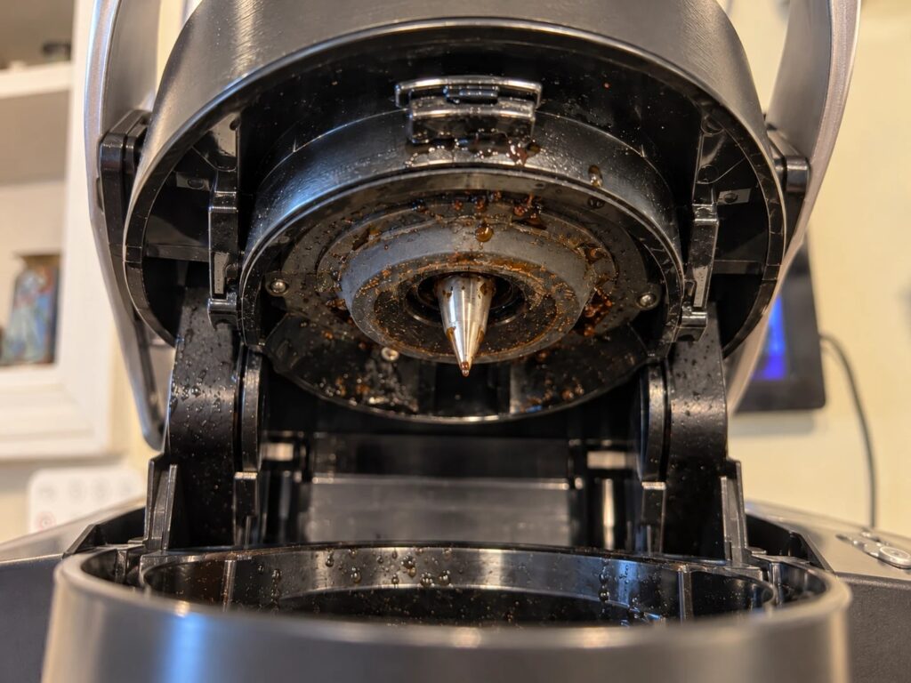 Handle up, looking at the underside of the brew head: the entrance needle and the coffee splatter around it.